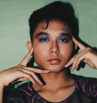 Vibrant portrait of a young Asian model with colorful eye makeup and stylish attire.