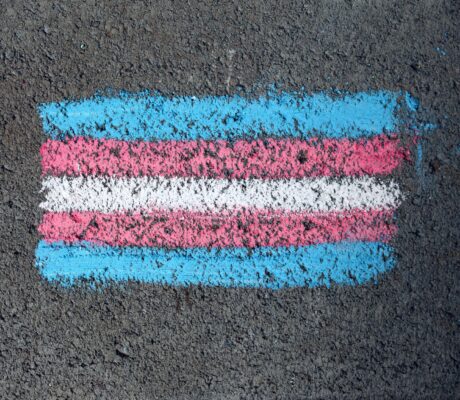 Close-up of a transgender pride flag chalk drawing on rough pavement surface.