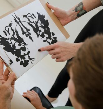 Hands holding a clipboard with an inkblot for psychological analysis.