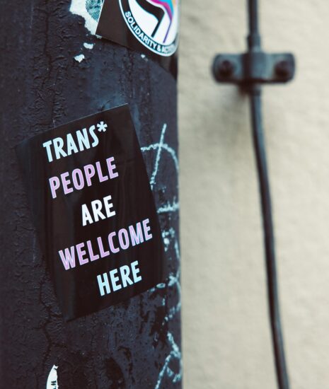 Sticker with message 'Trans people are welcome here' on an urban pole, promoting inclusivity.