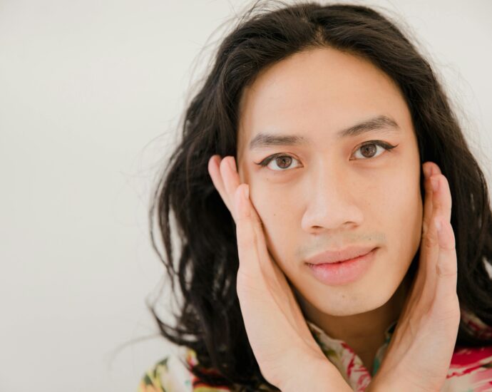 Close-up portrait of an expressive person with artistic eyeliner and colorful attire.